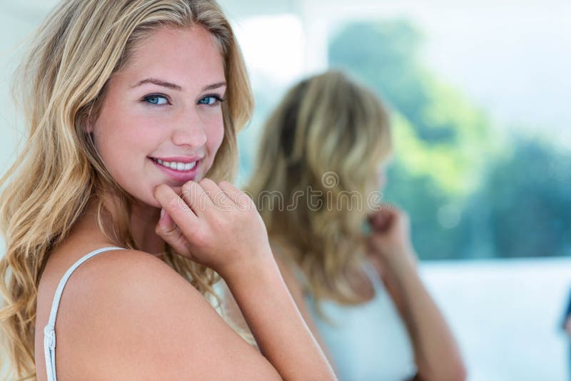 Smiling beautiful young woman looking at herself in the bathroom mirror