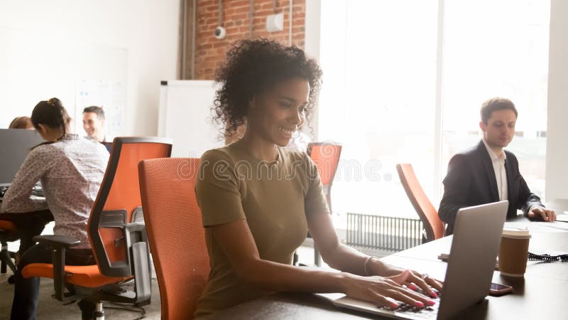 Smiling black female employee working on laptop in shared office stock image Smiling black female employee working on laptop in shared office stock image