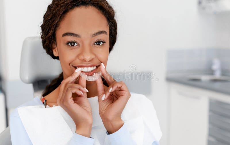 Smiling black girl holding invisible aligner, modern teeth trainer