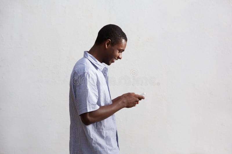 Side portrait of a smiling black guy walking and using mobile phone