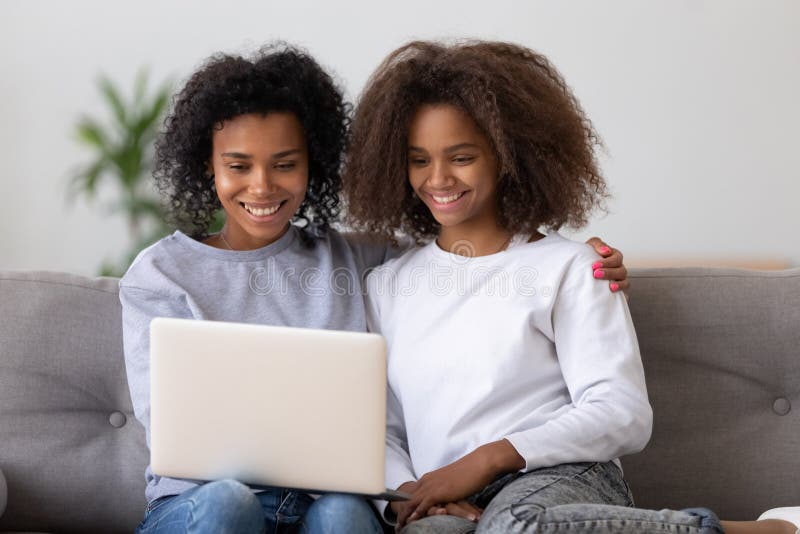 Smiling black mom and daughter watch video on laptop