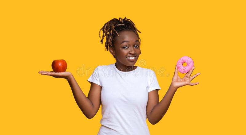 Smiling black woman looking at camera, having apple and donut