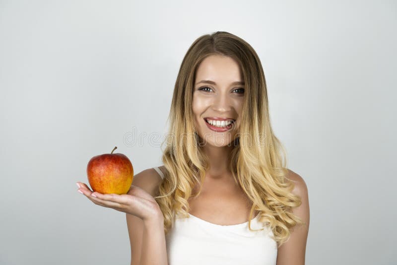 Smiling blond attractive woman holding juicy red apple in one hand isolated white background