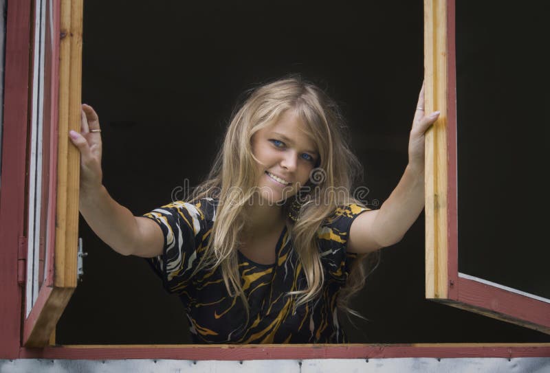 Smiling blond girl opening leaves of a window