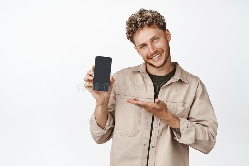 Smiling blond man demonstrating a mobile app, holding smartphone and showing on smartphone screen, standing over white