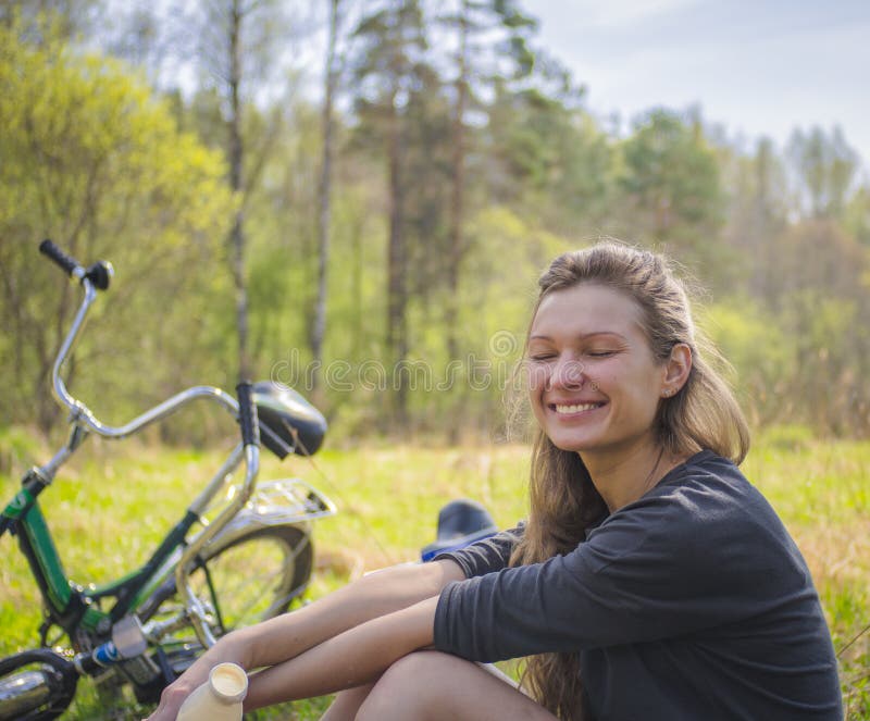 Smiling blond woman resting while sitting on the lawn while walking on a bike