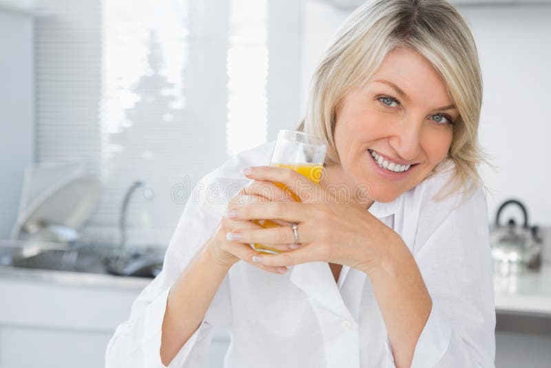 Smiling blonde having orange juice in kitchen