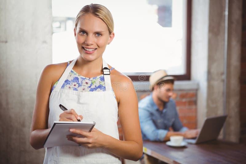 Portrait of smiling blonde waitress taking order in front of customer at coffee shop