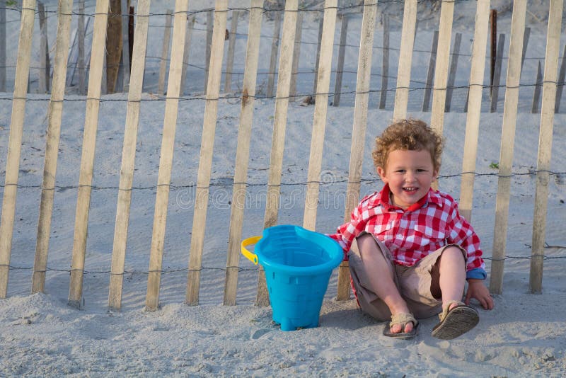 Smiling Boy on Beach in Front of Wooden Fence