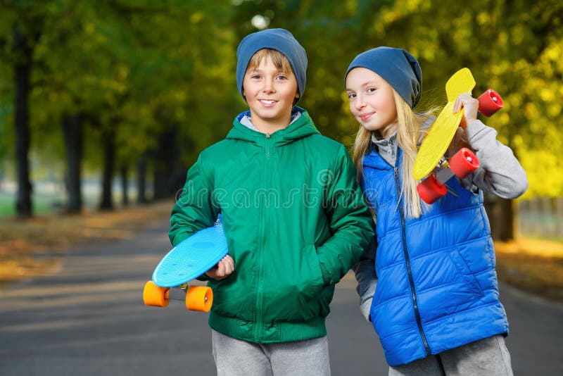 Smiling boy and girl holding color plastic penny boards or skateboards outdoor.