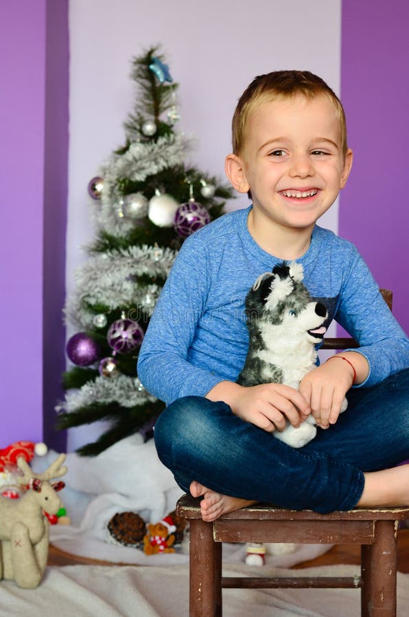 Chico ronco el perro juguete sobre el de madera una silla más cercano árbol de navidad.