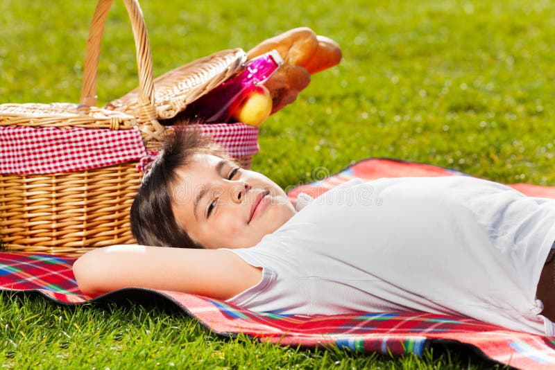 Smiling boy laying on grass next to picnic basket