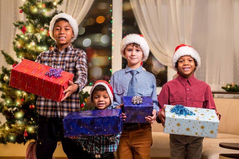 Smiling boys holding Christmas presents. Kids with presents beside spruce. Joyful holiday atmosphere at home. Let the good times roll.