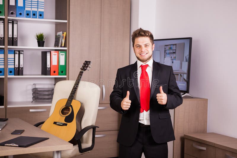 Smiling businessman in black suit and ret tie showing thumbs up