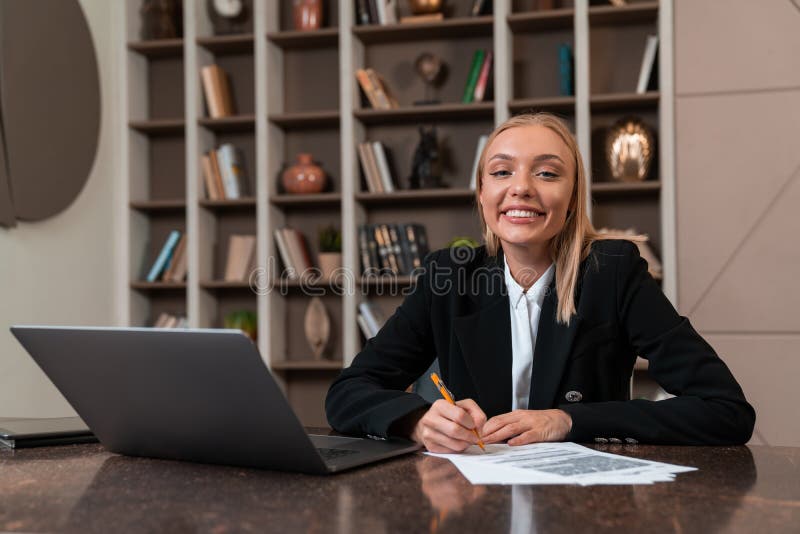 Smiling businesswoman with pen in hand, laptop in office room stock photos