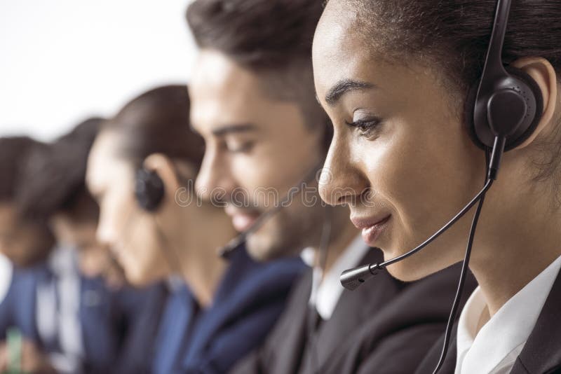 Smiling call center operator in headset working with colleagues behind stock images Smiling call center operator in headset working with colleagues behind stock images