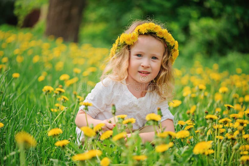 Smiling child girl in dandelion wreath on spring flower field