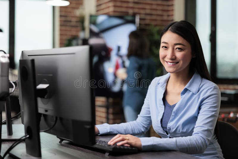 Smiling company employee sitting at desk in office workspace while looking at camera. stock photography