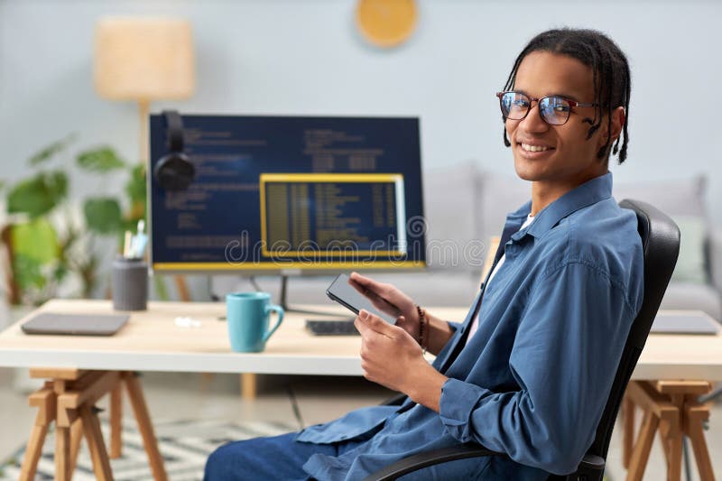 Smiling computer programmer holding tablet and writing code at workplace stock photography