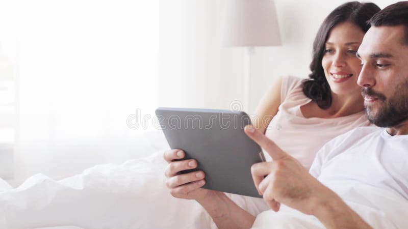 Smiling couple in bed with tablet pc computer