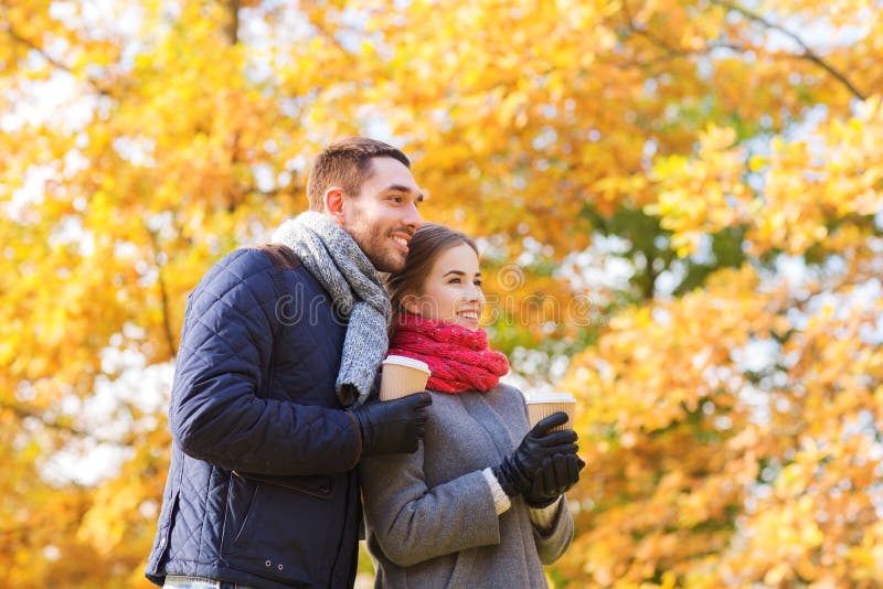 Smiling couple with coffee cups in autumn park