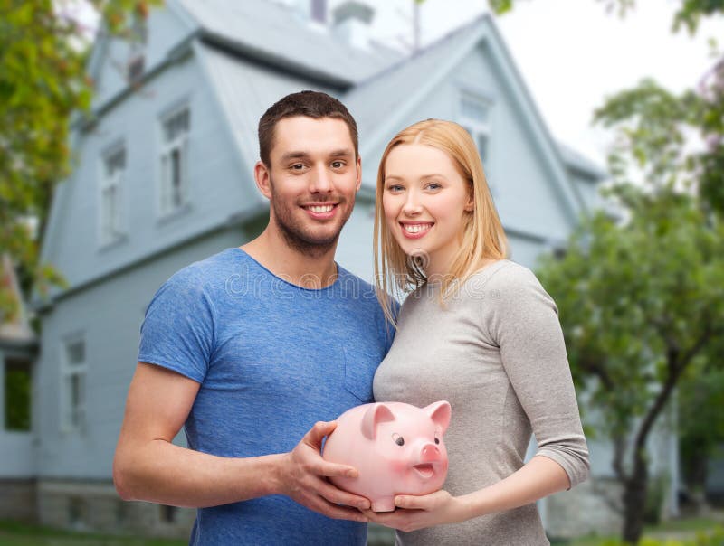 Smiling couple holding piggy bank over house stock photo Smiling couple holding piggy bank over house stock photo