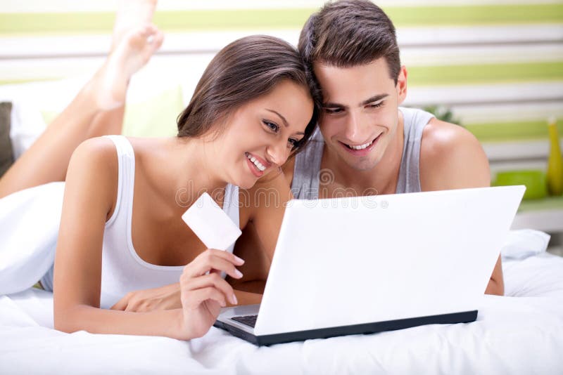 Happy young couple shopping online while lying on their bed. Happy young couple shopping online while lying on their bed