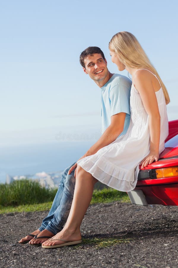 Smiling couple sitting on their cabriolet car hood.