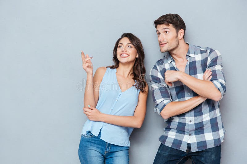 Smiling Couple Standing and Pointing at Something Over Gray Background ...