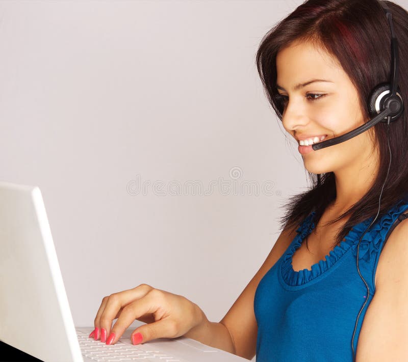 Attractive young smiling customer service woman answering call and entering information into computer