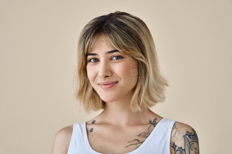 Smiling cute blonde girl pretty face and tattoos at beige background. Portrait.