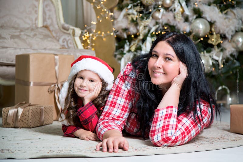 Smiling cute little girl with santa hat and mother near gifts and Christmas tree. New year or Christmas family celebration at home stock photos Smiling cute little girl with santa hat and mother near gifts and Christmas tree. New year or Christmas family celebration at home stock photos