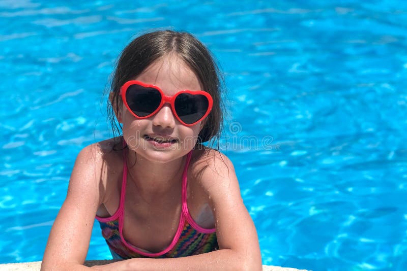 Smiling cute little girl in sunglasses in swimming pool on sunny day. Childhood and summer