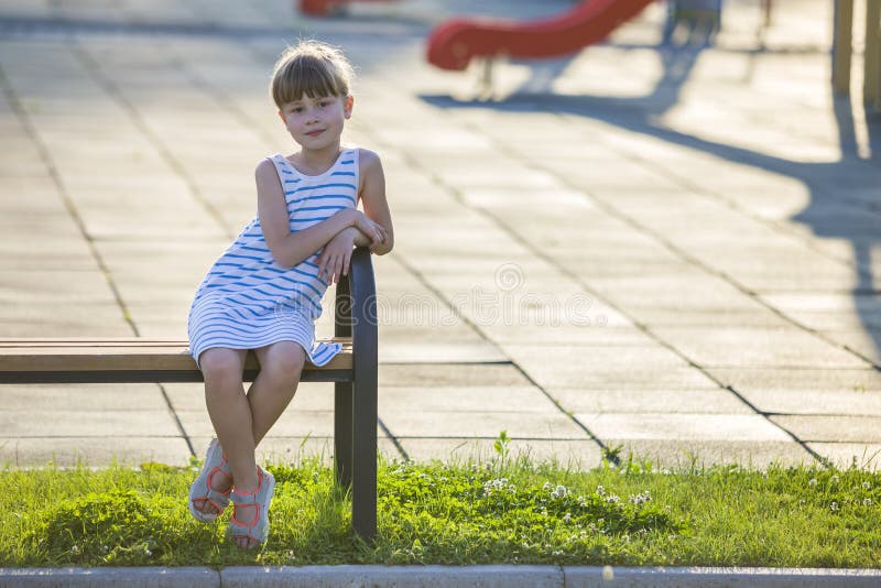 Smiling cute young girl sitting alone outdoors on bench on sunny summer day royalty free stock photography Smiling cute young girl sitting alone outdoors on bench on sunny summer day royalty free stock photography