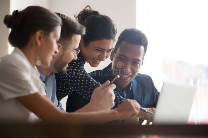 Smiling diverse colleagues laugh brainstorming using laptop stock photo Smiling diverse colleagues laugh brainstorming using laptop stock photo