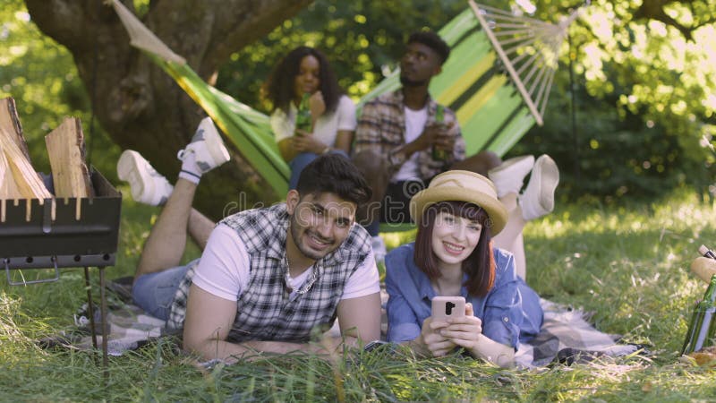 Four multiracial friends relaxing, chatting and drinking on picnic outdoors