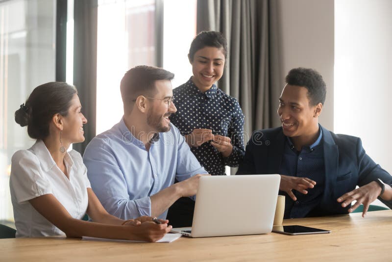 Smiling diverse employees talk brainstorming in office using laptop stock image Smiling diverse employees talk brainstorming in office using laptop stock image