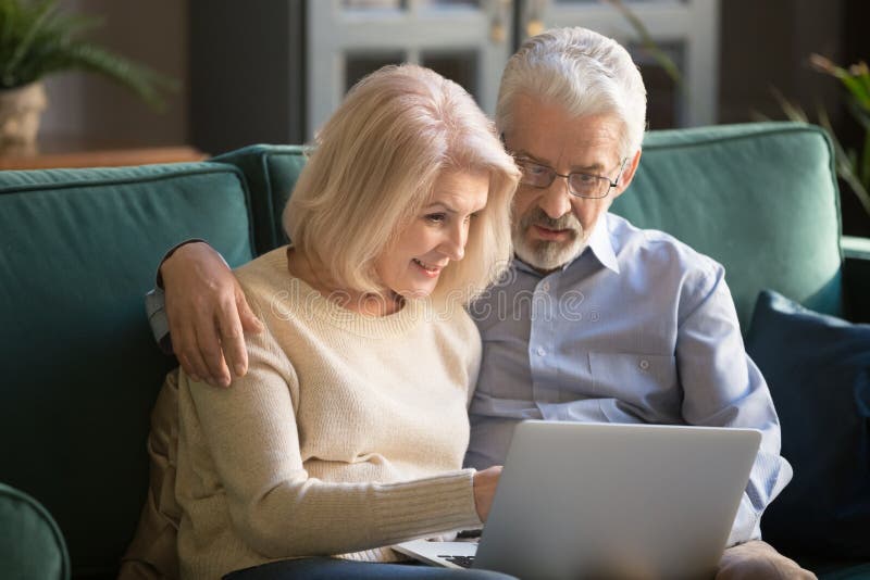 Smiling aged spouse spending free time on sofa with computer. stock photography Smiling aged spouse spending free time on sofa with computer. stock photography