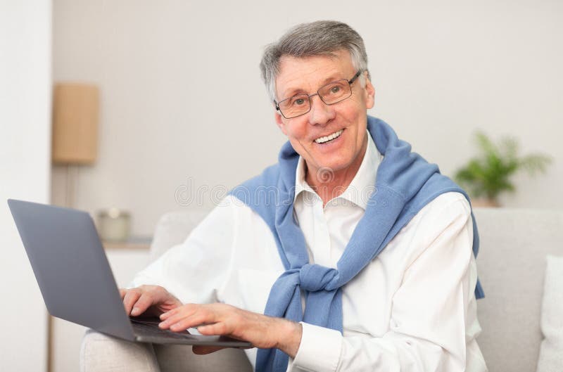 Elderly Man Working on Laptop Sitting on Couch at Home Stock Photo