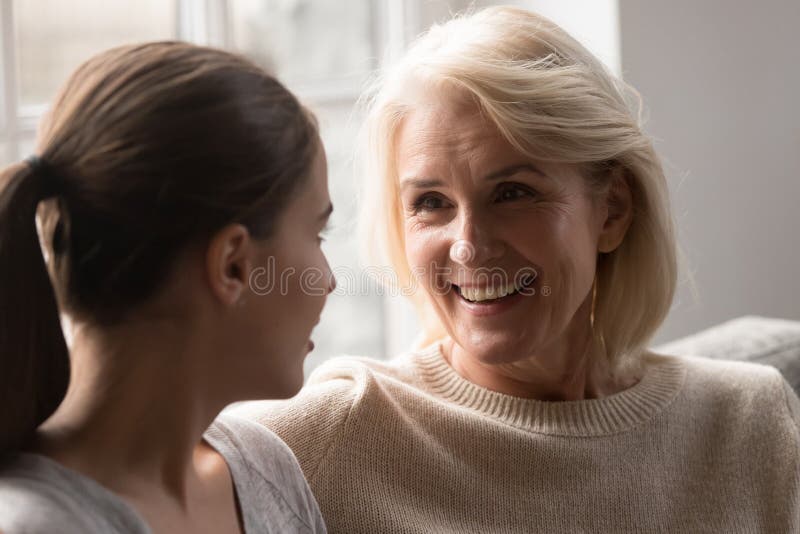 Smiling elderly mother and adult daughter chat at home