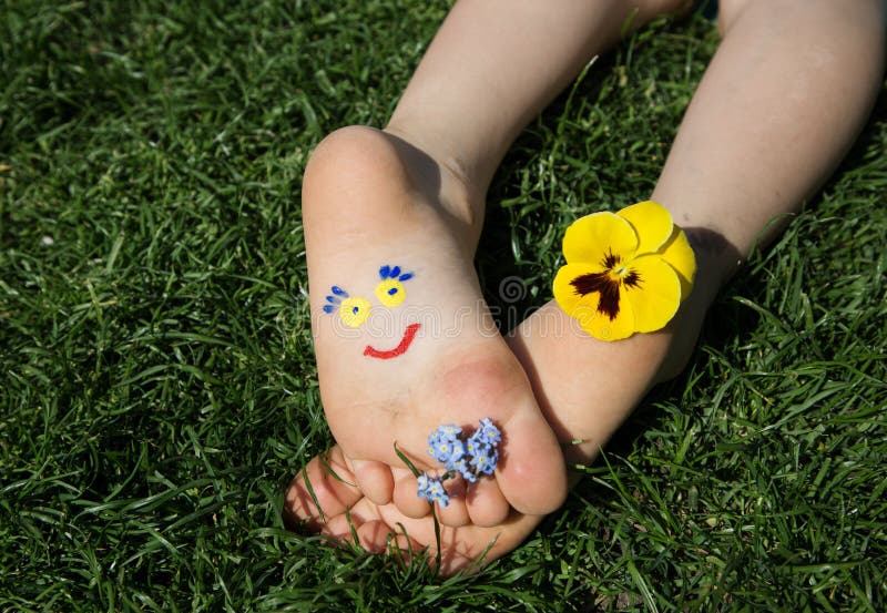 Smiling face painted on children`s bare feet, yellow and blue flowers