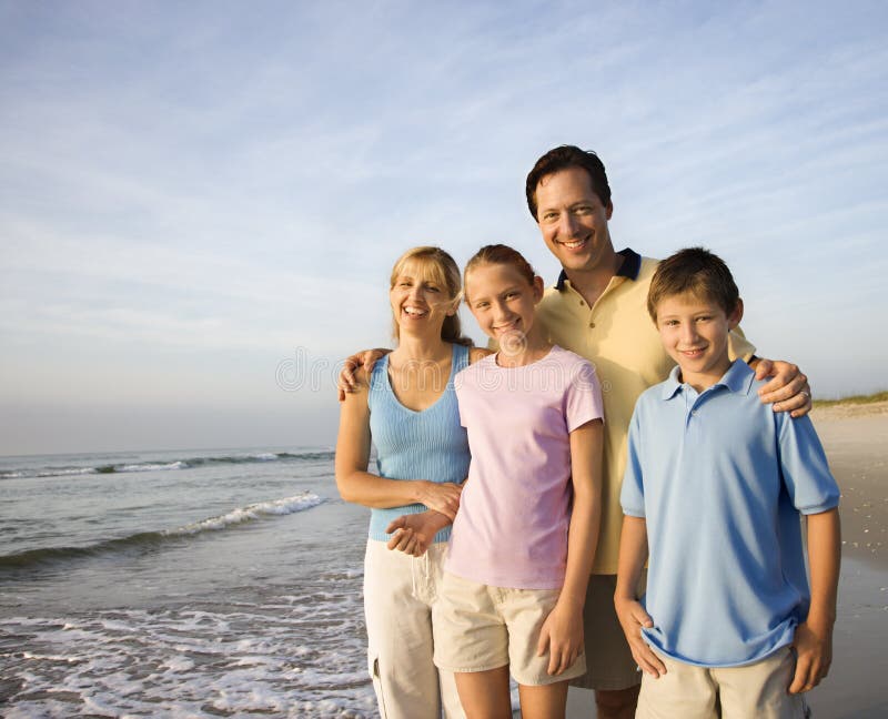 Ritratto di Caucasica famiglia di quattro persone in posa sulla spiaggia guardando il visualizzatore di sorridere.