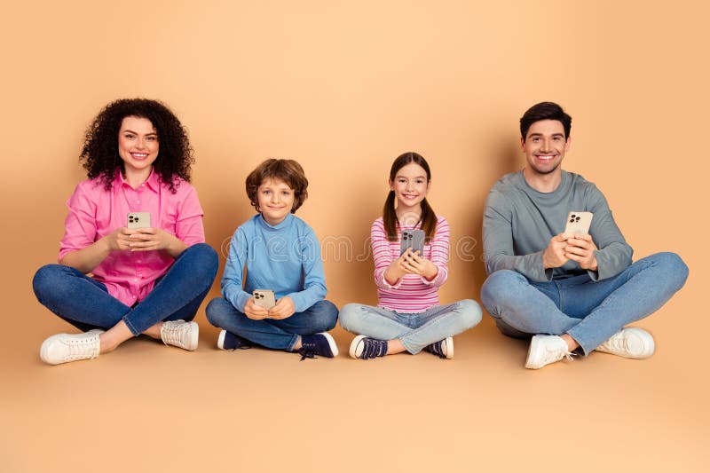 Smiling Family Sitting on a Beige Background Using Smartphones and Bonding Together, Representing Modern Relationships royalty free stock image