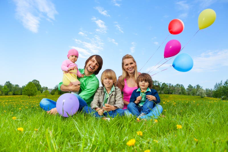 Smiling family sitting on green grass with flying balloons in summer. Smiling family sitting on green grass with flying balloons in summer