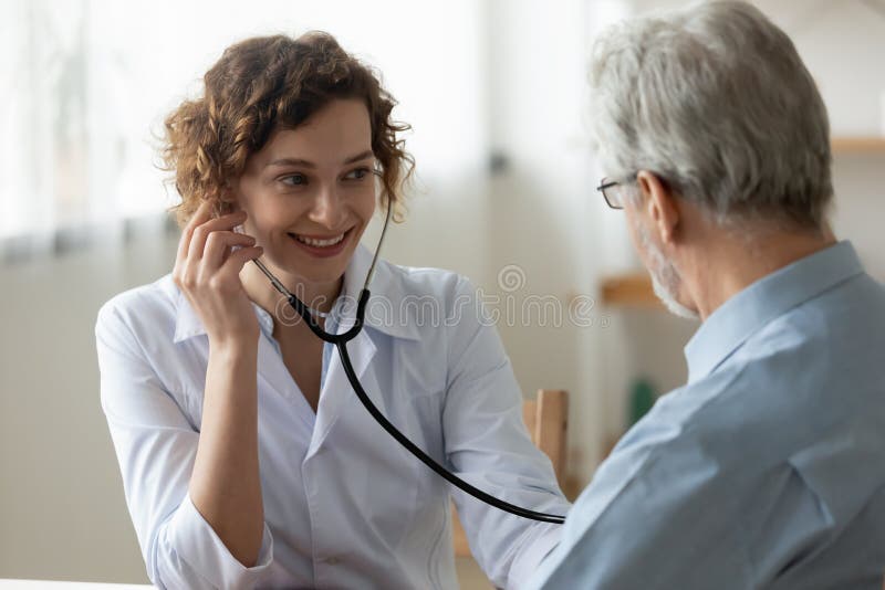 Smiling female nurse listen to heart of elderly patient