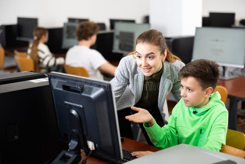 Smiling Female Teacher Talking To Happy Preteen Student In Computer