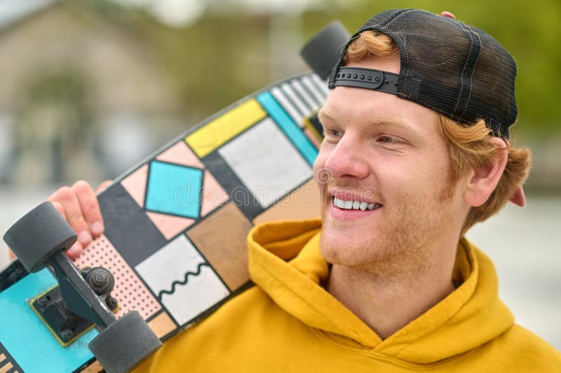 Smiling ginger young guy with skateboard looking contented stock photos