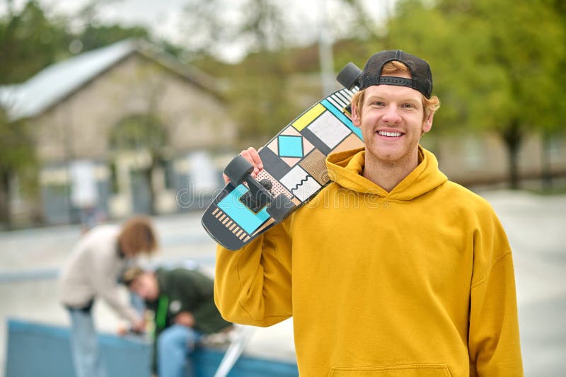 Smiling ginger young guy with skateboard looking contented stock images