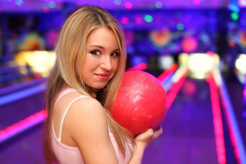 Smiling girl with ball stands in bowling club