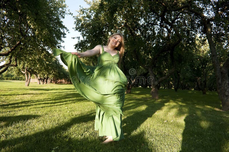 Smiling girl dance in green dress in park